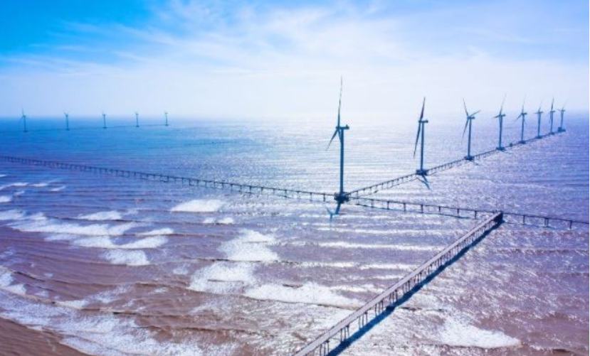 Rows of offshore wind turbines linked by access trestles in shallow coastal water